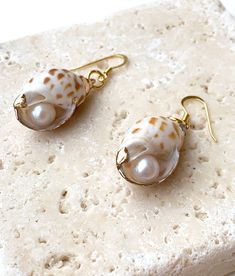 two seashells are sitting on top of a piece of white marble with gold earwires