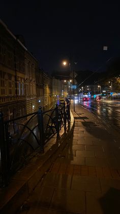 two people standing on the side of a street next to a fence at night time