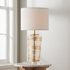 a table with a lamp on top of it next to a white wall and window