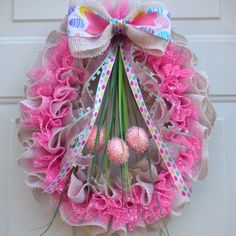 a pink and white wreath hanging on the front door with easter eggs attached to it