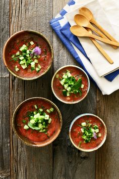 three bowls filled with soup and garnished with cucumbers, on top of a wooden table