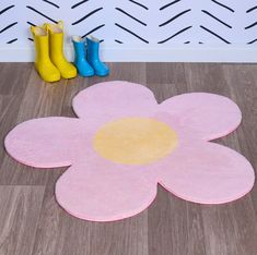 a pink rug with a yellow center and two blue rubber boots on the floor next to it