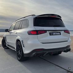 the rear end of a white mercedes gle suv parked on a beach near the ocean