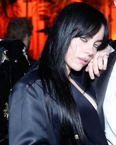 a woman with long black hair wearing a suit and holding her hand up to her ear