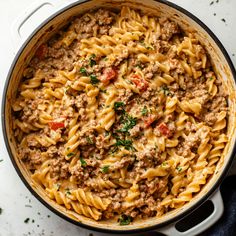 a pot filled with pasta, meat and parsley on top of a white table