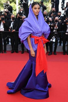 a woman in purple and red is standing on a red carpet with cameras around her