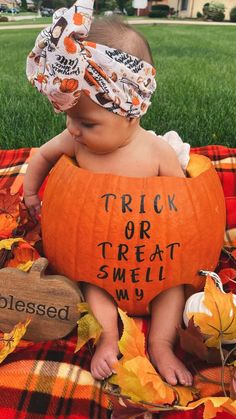 a baby in a pumpkin costume sitting on a blanket with a trick or treat sign