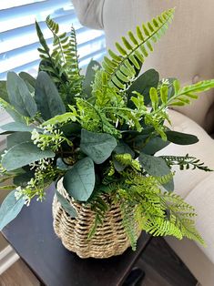 a basket filled with lots of green plants on top of a table next to a couch