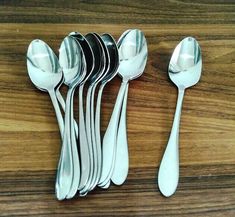 six spoons are lined up on a wooden table with silverware in the middle