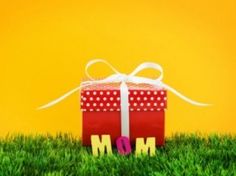 a red gift box sitting on top of green grass with the word mom written in it