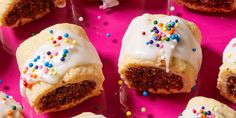 several pastries with white frosting and sprinkles on a pink surface