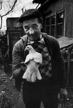 an old man holding a white bird in his right hand and looking at the camera