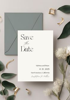 the save the date card is surrounded by greenery and gold foil on top of an envelope