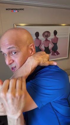 a bald man in a blue shirt is holding his neck