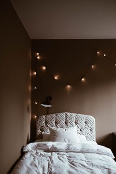 a bed with white linens and lights on the wall above it in a bedroom