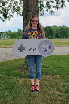 a girl holding up a nintendo wii controller cardboard cutout in front of a tree