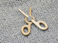 a pair of wooden scissors sitting on top of a gray knitted surface with yarn