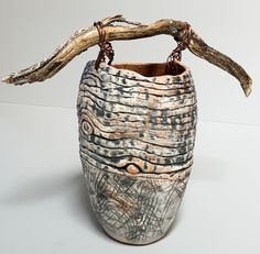 a ceramic vase with a branch hanging from it's side on a white surface