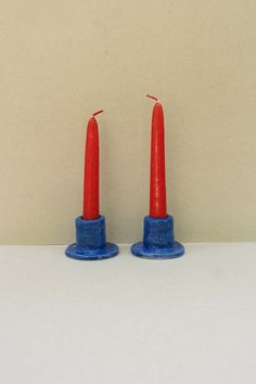 two red candles sitting on top of each other in front of a white wall and floor