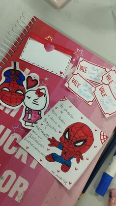 a pink notebook with spiderman stickers on it and some pens next to it