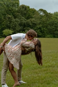 a man and woman kissing in a field with trees in the backgrouds