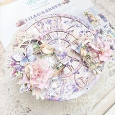 a close up of a clock on a table with paper flowers and other things around it