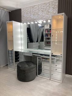 a white vanity with drawers and lights on the top shelf is next to a round ottoman