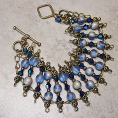 "Beaded bracelet drapes gracefully over your wrist with a mix of cobalt blue AB bi cone crystal beads and round blue glass beads accented with antique brass beads. Wire wrapped segments of beads are linked on antique brass chain. Bracelet closes with a matching antique brass metal toggle closure. This bracelet has a slinky fit and the blue beads have a brilliant AB quality to them. Length of the bracelet is 7 1/2\" (19.5 cm) and the width is 1 1/4\". Let me know prior to shipping if you need an Blue Czech Glass Bracelet With Spacer Beads, Blue Czech Glass Beaded Crystal Bracelet, Bohemian Blue Czech Glass Bracelets, Blue Bohemian Metal Bracelets, Elegant Blue Metal Beaded Bracelets, Bohemian Blue Metal Bracelets, Elegant Blue Beaded Metal Bracelets, Bohemian Blue Metal Bracelet, Blue Czech Glass Bracelets With Spacer Beads