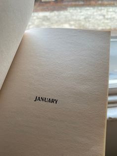 an open book with the word january written on it, in front of a window