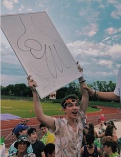 a man holding up a sign while standing in front of a group of people on a field