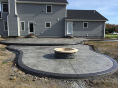 a concrete patio with a fire pit in front of a large gray house on a sunny day