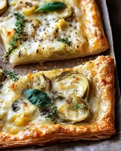 two square pizzas with artichoke and spinach toppings, one is cut in half