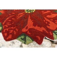 a red rug with green and yellow flowers on top of stone floor next to rocks