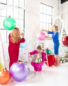 two women and one child are playing with balloons in front of christmas decorations, while another woman stands behind them