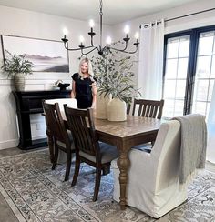 a woman standing in front of a dining room table with chairs and a piano behind her