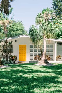 a yellow door sits in the front yard of a white house with palm trees around it