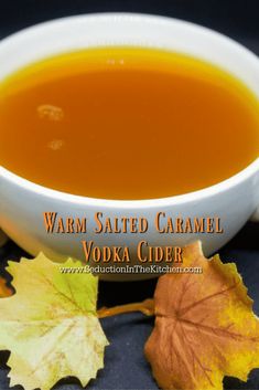 a white bowl filled with orange liquid next to some autumn leaves on a black surface