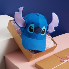 a blue hat sitting in a cardboard box on top of a pink table next to a brown package