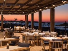 an outdoor restaurant with tables and chairs overlooking the ocean at sunset or sunrise, along with lights on