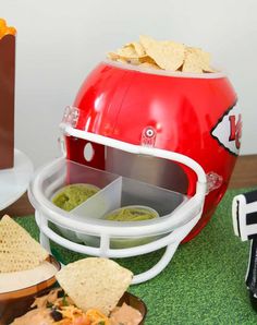 a football helmet is sitting on a table with chips and guacamole in it