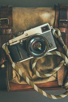 an old camera sitting on top of a brown leather bag with a rope around it