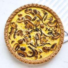 a quiche with mushrooms and cheese in a pie crust on a white tablecloth