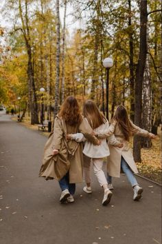 three girls are walking down the street in an autumn park with their arms around each other