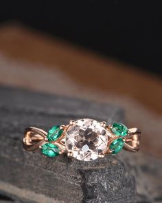 a ring with an oval cut diamond and green stones on it, sitting on top of a rock