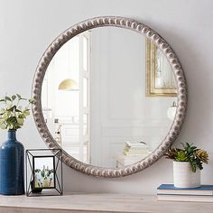 a round mirror sitting on top of a wooden table next to a vase with flowers