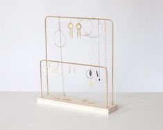 a gold jewelry display with earrings and necklaces hanging from it's sides on a white surface