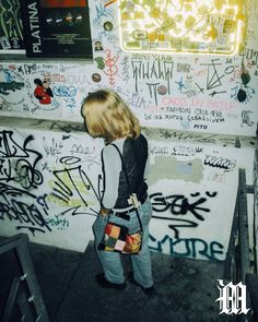 a young woman standing in front of a wall covered with graffitti and neon lights