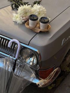 an old car with flowers and coffee cups on the hood