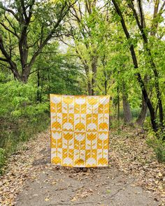 a yellow and white quilt sitting on the side of a road in front of trees