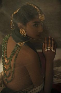 a woman wearing green jewelry and holding her hand up to her face